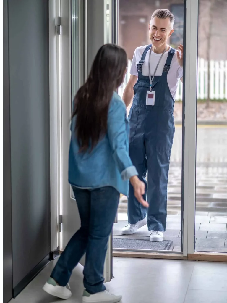 Kundin öffnet die Wohnungstür; Techniker in Arbeitskleidung begrüßt sie freundlich – diskrete Vor-Ort-Besichtigung und Beratung.