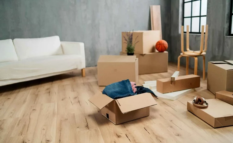 Moderner Raum mit Kartons; offene Kiste mit Kleidung und Alltagsgegenständen – geordnete Auflösung eines Haushalts.
