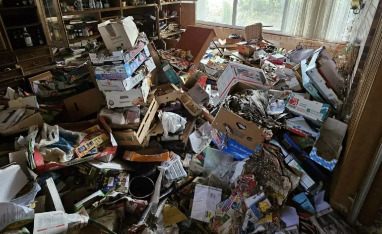 Wohnzimmer einer stark überfüllten Messie-Wohnung mit Kartons, Papierstapeln und Haushaltsgegenständen vor der Entrümpelung.