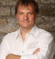 Portrait eines Mitarbeiters vor Steinwand, weißes Hemd – Ansprechpartner für Entrümpelung und Haushalts-/Firmenauflösung in Würzburg.