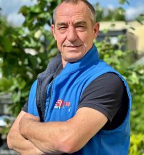 Mitarbeiter im blauen Arbeitsgilet mit verschränkten Armen im Grünen – Teamfoto von Efi Transporte in Würzburg.