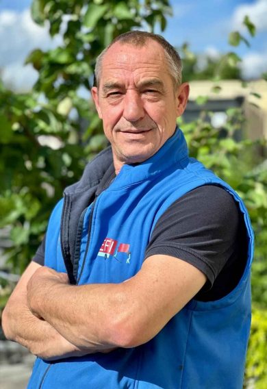 Mitarbeiter im blauen Arbeitsgilet mit verschränkten Armen im Grünen – Teamfoto von Efi Transporte in Würzburg.